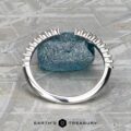 The "Kivu" band in 18k white gold stands upright before a rough blue stone on a gray, patterned surface. "Earth's Treasury" is displayed at the bottom.