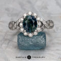 The "Passiflora" ring in 14k white gold features a 2.48-carat Australian sapphire, accented with small clear stones and displayed on a blue mineral, with the Earth’s Treasury logo shown below.