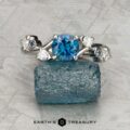 A platinum "Jasmine" ring with a 1.05-carat Montana sapphire centerpiece, accented by diamonds, rests on a rough blue stone. The "EARTH'S TREASURY" logo and text are displayed at the bottom.