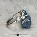 The "Jasmine" ring in platinum with a 1.05-carat Montana sapphire is shown leaning against a rough blue stone on a textured gray surface, branded "Earth's Treasury.