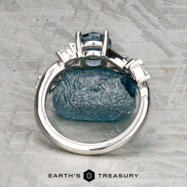 The "Jasmine" ring in platinum with 1.05-carat Montana sapphire The "Jasmine" ring in platinum with a 1.05-carat Montana sapphire rests on a rough blue stone atop a textured gray surface, with the Earth's Treasury logo below—an elegant jewelry piece for any occasion.