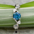 The "Jasmine" ring in platinum features a 1.05-carat Montana sapphire center, accented by smaller clear and blue stones for floral elegance. Displayed on green leaves with the Earth's Treasury logo below.