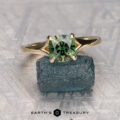 The "Cybele" ring in 14k yellow gold with a 1.58-carat Australian sapphire rests on a green crystal atop a metallic patterned surface, with the "Earth's Treasury" logo below.
