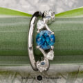 The "Jasmine" ring in platinum, featuring a 1.05-carat Montana sapphire and custom-fit contour band, is displayed on a green leaf. The "Earth's Treasury" logo appears below, highlighting this elegant gemstone ring set.