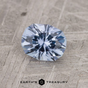 A 1.18-Carat Light Violet Blue Montana Sapphire is showcased on a textured gray surface, featuring the "Earth's Treasury" logo at the bottom.