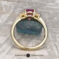 The "Dryope" ring in 18k yellow gold showcases a 1.41-carat Ceylon sapphire flanked by two diamonds, displayed upright on textured blue stone with the Earth's Treasury logo below. Inspired by the enchanting Dryope collection.