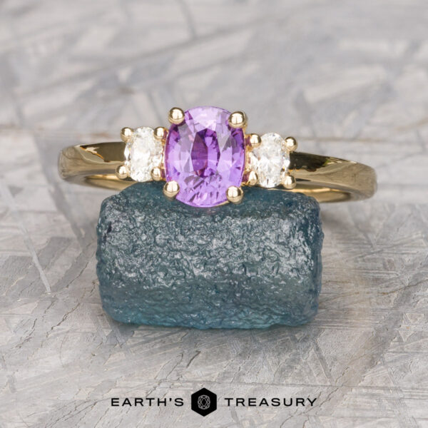The "Dryope" ring in 14K yellow gold with 1.03-carat Madagascar sapphire The "Dryope" ring features a 1.03-carat Madagascar sapphire set in 14K yellow gold, flanked by two clear stones and displayed on a rough blue crystal with "Earth's Treasury" beneath.