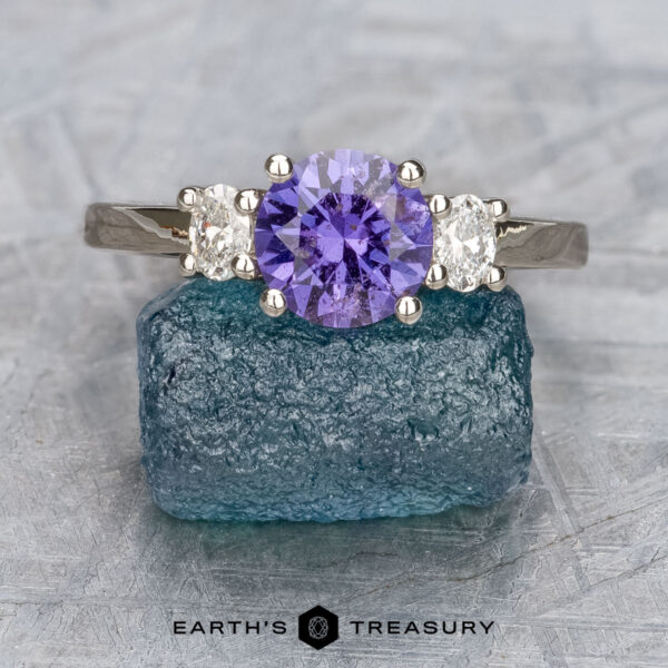 The "Dryope" ring in platinum with 1.13-carat Umba sapphire The "Dryope" ring in platinum, featuring a 1.13-carat Umba sapphire center stone, is displayed upright on a rough blue gemstone, highlighting the unique charm of this elegant three-stone design.