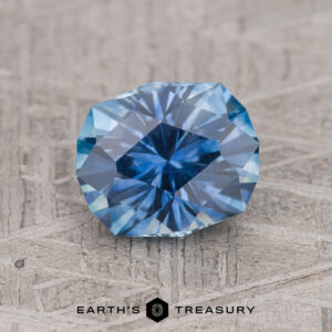 A 1.86-carat Medium Blue Montana Sapphire (Heated) is displayed faceted on a textured surface with the Earth’s Treasury logo beneath it.