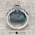 The "Minthe" ring in 14k white gold with a 1.39-carat Montana Sapphire is displayed upright against a rough blue stone on a textured gray surface. "EARTH'S TREASURY" is written below.
