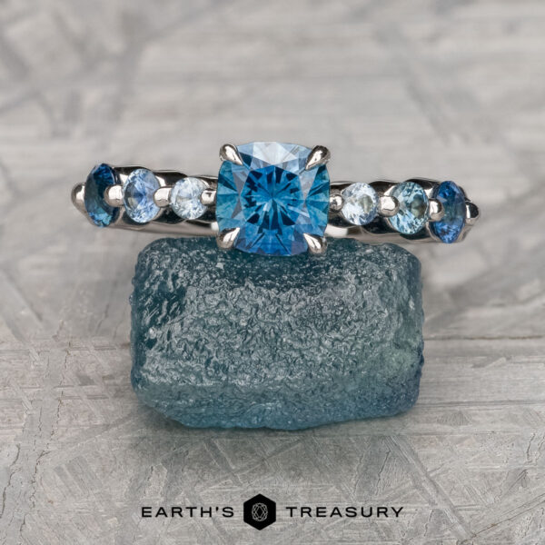 The "Minthe" ring in 14k white gold with 0.97-carat Montana sapphire The "Minthe" ring in 14k white gold showcases a 0.97-carat cushion-cut Montana sapphire centerpiece with round blue side stones, set atop a rough blue crystal and branded below with "Earth's Treasury.