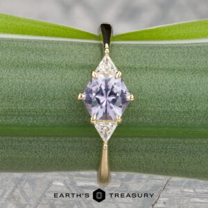The "Melilai" ring in 14k yellow gold features a 1.06-carat Montana sapphire and two clear stones, elegantly displayed on a green leaf with the Earth's Treasury logo below.