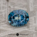 A 1.71-carat teal blue Montana Sapphire (heated) rests on a textured gray surface with the "EARTH'S TREASURY" logo below it.