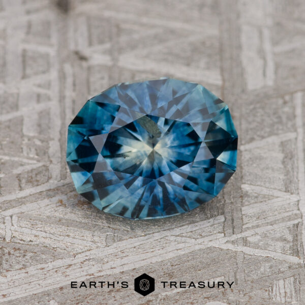 1.71-Carat Teal Blue Montana Sapphire (Heated) A 1.71-carat teal blue Montana Sapphire (heated) rests on a textured gray surface with the "EARTH'S TREASURY" logo below it.