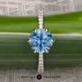 The Pave "Anemone" ring, featuring a 1.82-carat Montana sapphire set in 14k white gold, is displayed on a green stem. The "Earth's Treasury" logo appears at the bottom, showcasing this elegant piece.