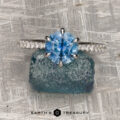 The Pave "Anemone" ring in 14k white gold with a 1.82-carat Montana sapphire is displayed on rough blue stone over a textured gray surface, highlighting its stunning design and exceptional jewelry craftsmanship.