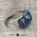 The Pave "Anemone" ring in 14k white gold, set with a 1.82-carat Montana sapphire, displayed as fine jewelry beside a rough blue crystal on textured gray; logo shows "Earth's Treasury.