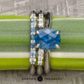 The "Anastasia" ring in platinum with a 2.34-carat Montana Sapphire, paired with the "Blies" and "Yonne" platinum bands, is displayed vertically on a green and white plant stem, with the "Earth's Treasury" logo below.