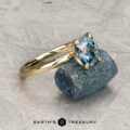 The "Alyssum" ring in 14k yellow gold with a 1.63-carat Montana sapphire rests on a rough blue crystal, with "Earth's Treasury" text below on a textured surface.