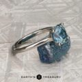 A platinum "Cathedral" ring with a 2.16-carat Montana sapphire is set atop a rough blue stone on a patterned gray surface, highlighting its elegance. The Earthās Treasury logo appears at the bottom.