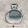 The "Cathedral" ring in platinum with a 2.16-carat Montana sapphire stands upright before a rough blue crystal on textured light gray, evoking solitaire card game elegance. "Earth's Treasury" is displayed at the bottom.