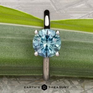 The "Cathedral" ring in platinum, featuring a 2.16-carat Montana sapphire solitaire, stands upright on a green leaf. "EARTH'S TREASURY" is printed at the bottom of the image.