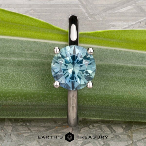 The "Cathedral" ring in platinum with 2.16-Carat Montana Sapphire The "Cathedral" ring in platinum, featuring a 2.16-carat Montana sapphire solitaire, stands upright on a green leaf. "EARTH'S TREASURY" is printed at the bottom of the image.