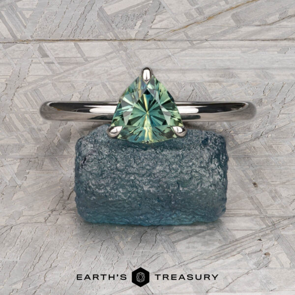 The "Alyssum" ring in platinum with 1.13-carat Australian sapphire The "Alyssum" ring, crafted in platinum and set with a 1.13-carat Australian sapphire, is displayed on a rough blue stone against a gray textured background, capturing refined elegance.