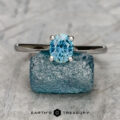 The "Cathedral" ring in 14K white gold with a 0.97-carat Montana sapphire stands upright on a rough blue crystal, set against a textured gray background, with the text "Earth's Treasury" below.