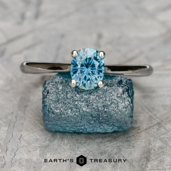 The "Cathedral" ring in 14K white gold with 0.97-carat Montana sapphire The "Cathedral" ring in 14K white gold with a 0.97-carat Montana sapphire stands upright on a rough blue crystal, set against a textured gray background, with the text "Earth's Treasury" below.