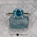 The "Cathedral" ring in platinum, featuring a 2.31-carat Australian sapphire, stands on a blue rough stone against a patterned background. The text "Earth's Treasury" appears below.