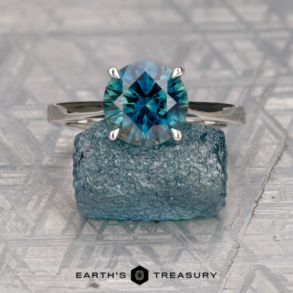 The "Cathedral" ring in platinum with 2.31-carat Australian sapphire The "Cathedral" ring in platinum, featuring a 2.31-carat Australian sapphire, stands on a blue rough stone against a patterned background. The text "Earth's Treasury" appears below.