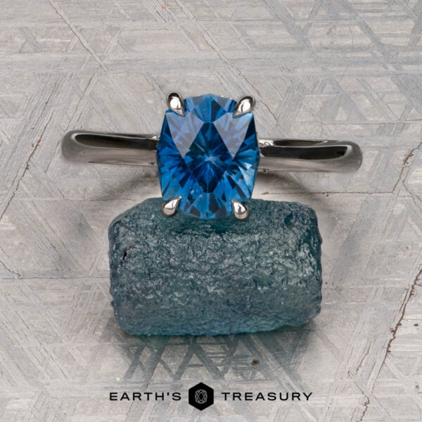 The "Anastasia" ring in platinum with 2.34-carat Montana sapphire The "Anastasia" ring in platinum with a 2.34-carat Montana sapphire is displayed on a rough blue stone against a patterned gray background, with "EARTH'S TREASURY" at the bottom.