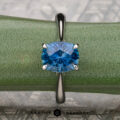 The Wetherell, Nikki and Yardy, Nicholas 5 ring features a blue gemstone in a four-prong silver Hidden Halo Solitaire setting, shown on a green textured surface with "Earth's Treasury" displayed at the bottom.