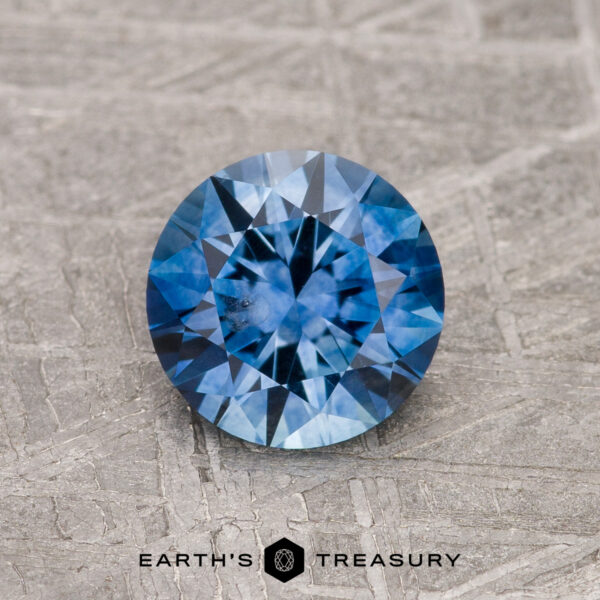 1.24-Carat Rich Blue Montana Sapphire (Heated) 1.24-Carat Rich Blue Montana Sapphire (Heated) with a round brilliant cut displayed on textured gray, featuring the "EARTH'S TREASURY" logo and text below.