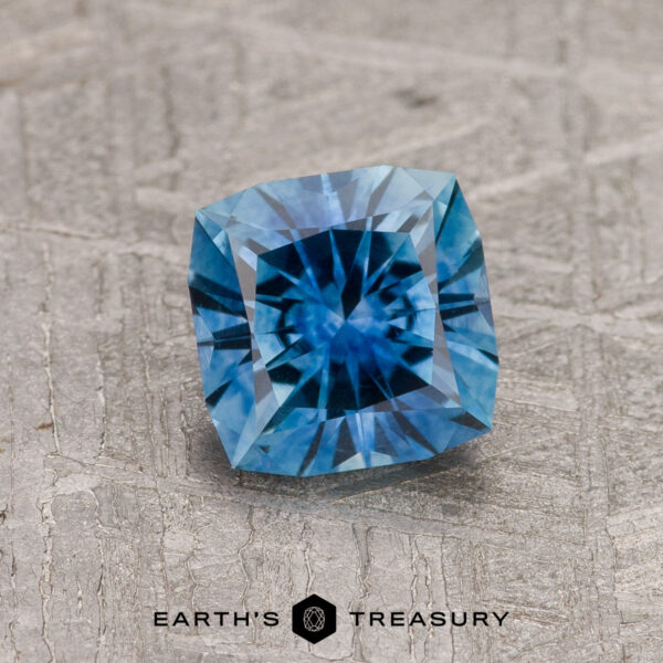1.19-Carat Peacock Blue Montana Sapphire (Heated) A 1.19-carat Peacock Blue Montana Sapphire (Heated), square-cut, is displayed on a textured gray surface featuring the "Earth's Treasury" logo at the bottom.