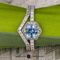 The “Ismene” ring in 14k white gold, featuring a 1.29-carat hexagon Montana Sapphire and petite pave diamond accents, is showcased on a green leaf with the "EARTH'S TREASURY" logo below.