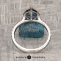The "Pleione" ring in 14K white gold with a 1.31-carat Montana sapphire is displayed upright on a textured gray surface, featuring the Earth's Treasury logo at the bottom.