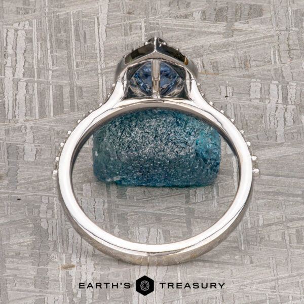 The "Pleione" ring in 14K white gold with 1.31-carat Montana sapphire The "Pleione" ring in 14K white gold with a 1.31-carat Montana sapphire is displayed upright on a textured gray surface, featuring the Earth's Treasury logo at the bottom.