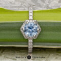 The "Ismene" ring in 14k white gold with a 1.29-carat Montana sapphire is displayed on a green leaf, featuring a diamond-encrusted band and the text "Earth's Treasury" below.