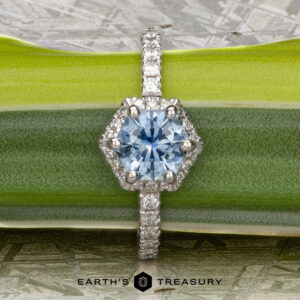 The "Ismene" ring in 14k white gold with a 1.29-carat Montana sapphire is displayed on a green leaf, featuring a diamond-encrusted band and the text "Earth's Treasury" below.