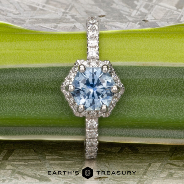 The “Ismene” ring in 14k white gold with 1.29-Carat Montana Sapphire The "Ismene" ring in 14k white gold with a 1.29-carat Montana sapphire is displayed on a green leaf, featuring a diamond-encrusted band and the text "Earth's Treasury" below.