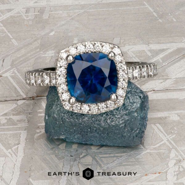 The Classic Pave Halo Ring in Platinum with 1.88-Carat Montana Sapphire The Classic Pave Halo Ring in Platinum features a 1.88-carat Montana sapphire center with sparkling clear accents, elegantly displayed on a rugged blue mineral backdrop.