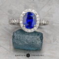 The Classic Pave Halo Ring in 14k white gold, featuring a 1.96-carat Madagascar sapphire surrounded by pavé stones, is displayed on rough blue mineral with "Earth's Treasury" text below.