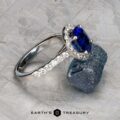 The Classic Pave Halo Ring in 14k white gold, showcasing a 1.96-carat Madagascar sapphire and diamond accents, rests on a rough blue stone, with the Earth’s Treasury logo displayed below.