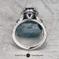 The Classic Pave Halo Ring in 14k white gold with a 1.96-carat Madagascar sapphire is displayed upright above a matching blue stone on a textured gray surface, with the "Earth's Treasury" logo at the bottom.