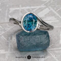 A platinum "Calliste" ring featuring a 1.66-carat Montana Sapphire is displayed on a rough blue stone, set against a geometric patterned background with the text "EARTH'S TREASURY" at the bottom.