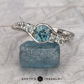 The "Venus" ring in 18K white gold with a 0.98-carat Montana sapphire is displayed atop a rough blue crystal, with "Earth's Treasury" appearing at the bottom.