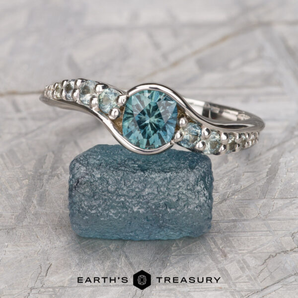 The "Venus" ring in 18K white gold with 0.98-carat Montana sapphire The "Venus" ring in 18K white gold with a 0.98-carat Montana sapphire is displayed atop a rough blue crystal, with "Earth's Treasury" appearing at the bottom.