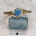 The "Calliste" ring in 18K yellow gold with a 1.08-carat Montana sapphire is displayed on a rough blue stone, with the "EARTH'S TREASURY" logo beneath—a striking example of fine gemstone jewelry.
